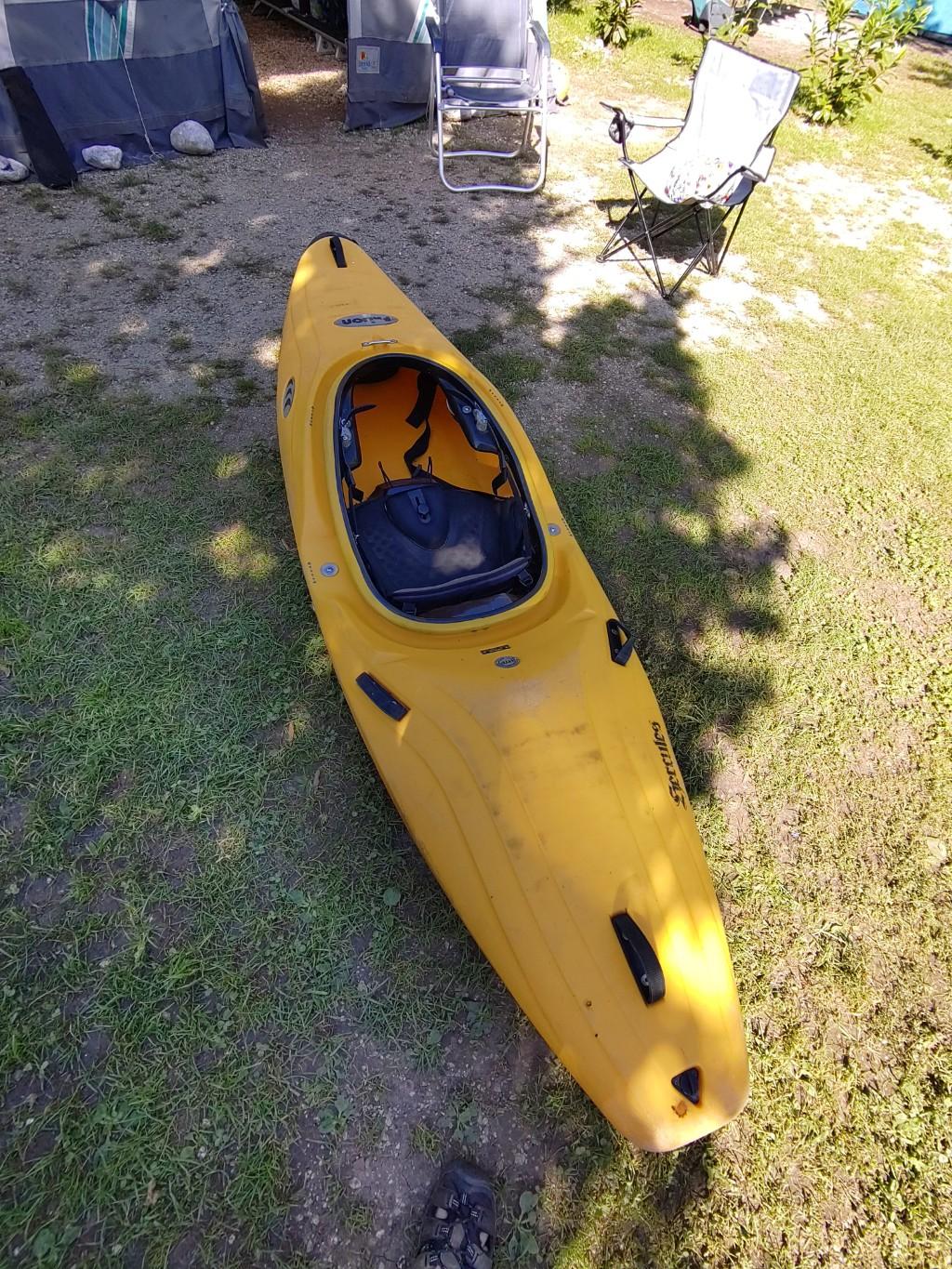 A yellow whitewater kayak in front of a tent