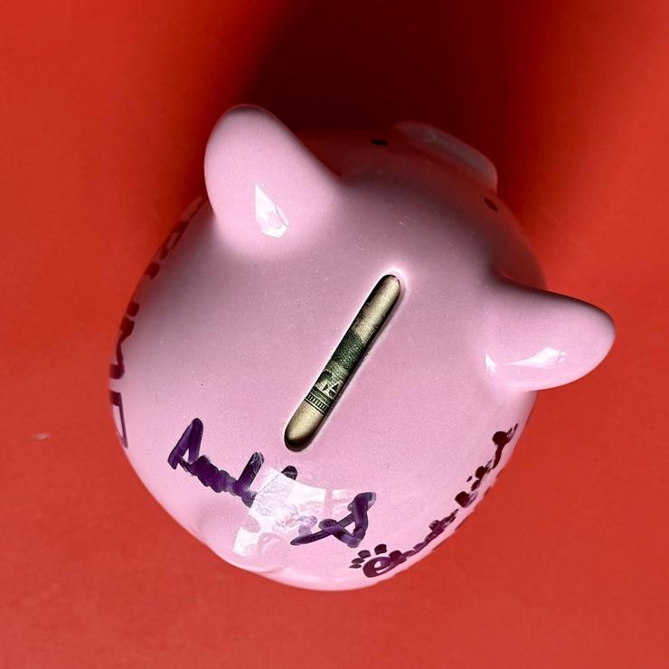 Top-view of a pink piggy bank that is full of quarters with a twenty dollar bill crammed in the top.
